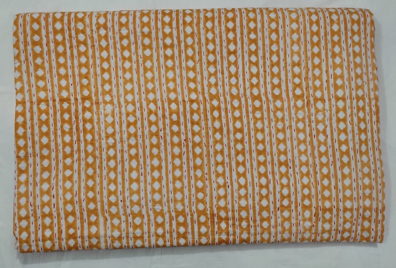 May include: A yellow and white fabric with a repeating pattern of small diamonds and thin lines. The fabric has a subtle texture and a slightly faded look.