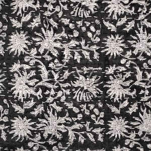 May include: A black fabric featuring a repeating white floral pattern of stylized chrysanthemums and leaves. The textile is detailed with horizontal rows of white running stitches that create a quilted texture across the entire surface.