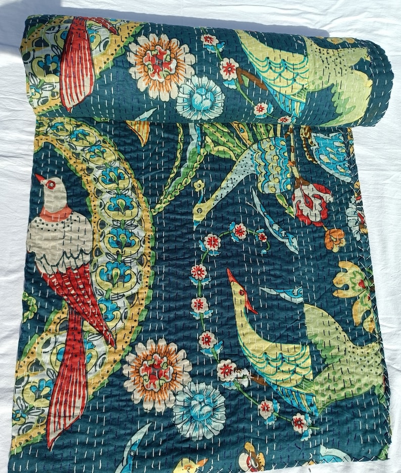 May include: A rolled-up, dark teal quilt with a vibrant bird and floral pattern. The design features birds with red, yellow, and white details, along with colorful flowers and leaves. The quilt is hand-stitched with white thread.