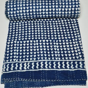 May include: A folded cotton quilt featuring a repeating pattern of white triangles on a deep blue background. The fabric displays horizontal bands of white wavy lines and solid blue sections, all accented with visible white running stitch quilting.