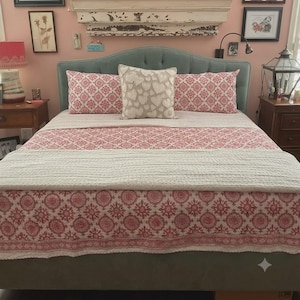 May include: A bed featuring a tufted, light blue upholstered headboard, two red and white patterned rectangular pillows, a central beige square pillow with a heart texture, and a matching red and white patterned quilt with a white textured throw.