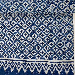 Op de afbeelding: Een blauwe en witte kantha-deken met een geometrisch patroon. De deken heeft een rand met een herhalend patroon van driehoeken en bomen.