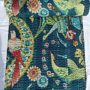 May include: A rolled-up, dark teal quilt with a vibrant bird and floral pattern. The design features birds with red, yellow, and white plumage, surrounded by colorful flowers and foliage. The quilt is hand-stitched with white thread.