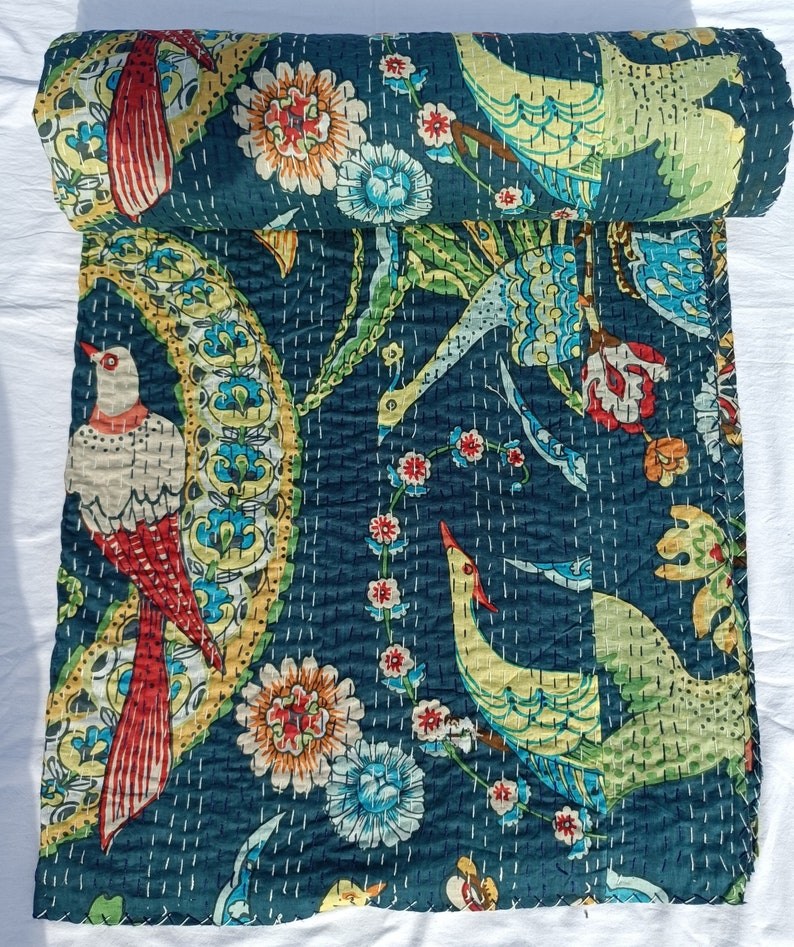 May include: A rolled-up, dark teal quilt with a vibrant bird and floral pattern. The design features birds with red, yellow, and white plumage, surrounded by colorful flowers and foliage. The quilt is hand-stitched with white thread.