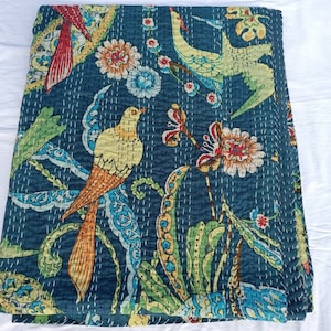 May include: A folded, dark teal quilt with a vibrant bird and floral pattern. The design features colorful birds with yellow, orange, and teal feathers, surrounded by flowers and foliage in shades of green, blue, and red. White stitching outlines the design.