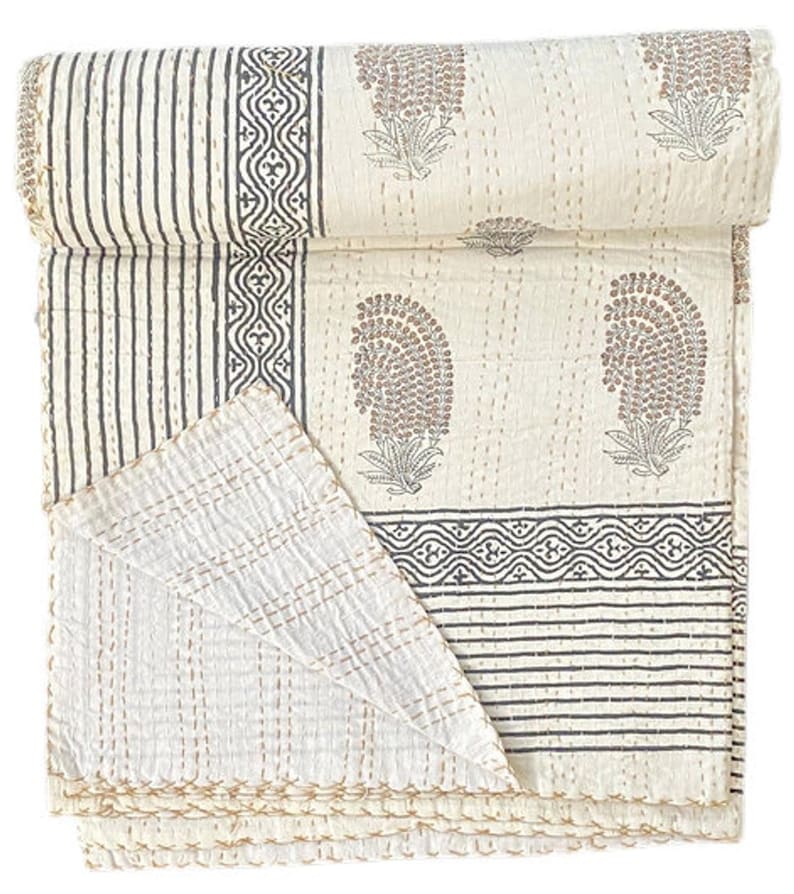May include: A folded off-white cotton quilt featuring a repeating pattern of brown paisley motifs, dark gray geometric borders, and vertical stripes. The textile is finished with visible running stitch embroidery in a light tan thread throughout.