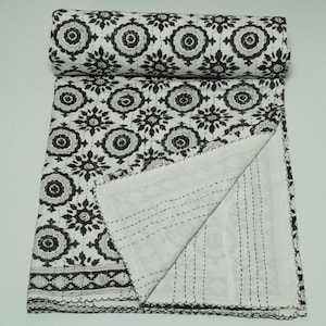 May include: A white and black patterned quilt with a rolled-up section. The quilt features a repeating floral design in black against a white background. The edges are finished with a black border and stitching.