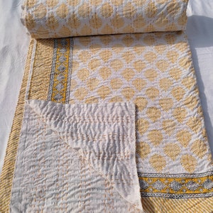 May include: A white and yellow quilt with a leaf pattern. The quilt is folded and rolled, showcasing the intricate stitching and design. The border features a geometric pattern with yellow and black accents. The quilt is made of soft, comfortable material.