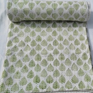 Può includere: Un trapunta di cotone bianco con un motivo a foglie verdi. La trapunta è piegata e arrotolata.