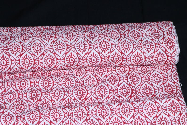 Pu&ograve; includere: Tessuto di cotone rosso e bianco con un motivo ripetitivo di fiori stilizzati. Il tessuto &egrave; piegato a met&agrave; e il motivo &egrave; visibile su entrambi i lati.