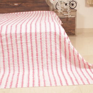 Puede incluir: Una colcha kantha rosa y blanca con un patrón de chevron. La colcha está doblada y drapeada sobre una cama.