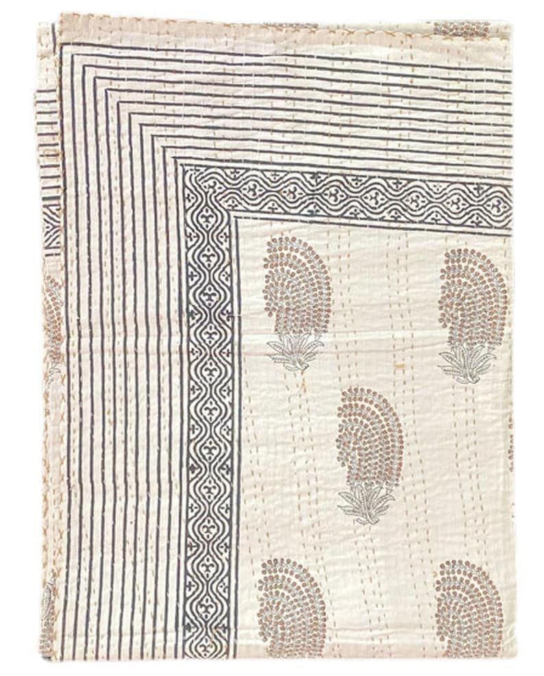 May include: A rectangular off-white cotton quilt featuring a repeating brown paisley-style floral pattern. The border consists of multiple thin dark brown parallel lines and a decorative geometric band. The fabric has visible running stitch details.