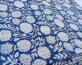 Puede incluir: Textil doblado con un patrón floral blanco repetido sobre un fondo azul oscuro. El diseño presenta grandes flores estilizadas y vides frondosas. La tela parece estar acolchada o cosida, creando una superficie texturizada.