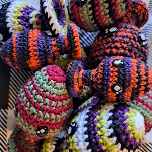 May include: A collection of colorful, crocheted octopus toys. Each octopus features a round head with button eyes and eight tentacles. The yarn colors include orange, purple, black, green, and white, creating a playful and whimsical appearance.