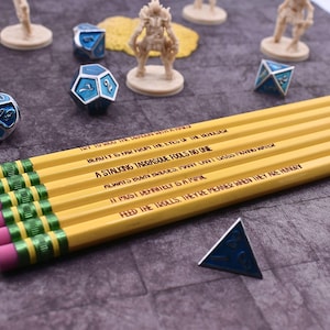 May include: A set of yellow pencils with green ferrules and pink erasers, each featuring black printed text including phrases like 'A STALKING TARRASQUE FOOLS NO ONE' and 'FEED THE TROLLS. THEY'RE MEANER WHEN THEY ARE HUNGRY', alongside blue polyhedral dice.