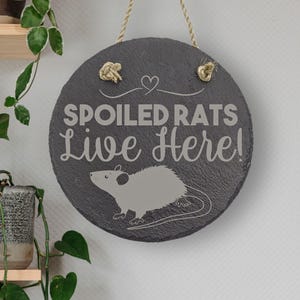 May include: A black slate sign with a rope hanger and the text "Spoiled Rats Live Here!" in white lettering. A gray rat illustration is below the text.