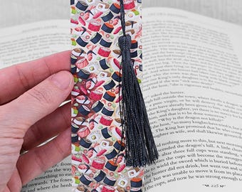May include: A colourful bookmark featuring a repeating pattern of sushi rolls. The bookmark is made of clear plastic and has a black tassel.