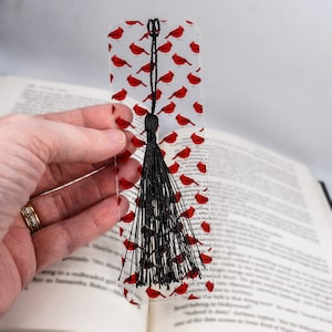 May include: A clear bookmark with a black tassel and a repeating pattern of red cardinals. The bookmark is approximately 6 inches tall.