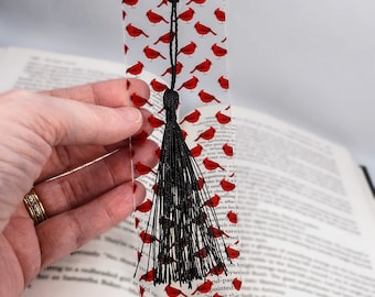 May include: A clear bookmark with a black tassel and a repeating pattern of red cardinals. The bookmark is approximately 6 inches tall.