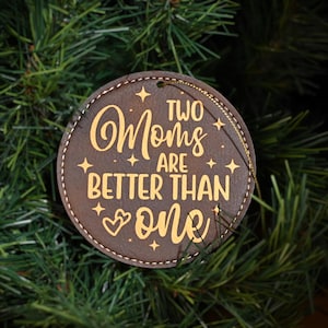 May include: A brown leather ornament with a gold inscription that reads "Two Moms Are Better Than One".