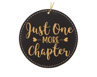 May include: Black leather ornament with gold stitching and the text "Just One More Chapter" in gold lettering.