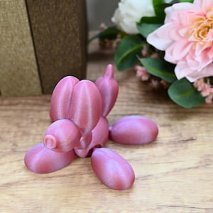 Puede incluir: Una escultura de animal de globo rosa en forma de perro. La escultura está hecha de un material brillante y metálico y tiene un aspecto realista.