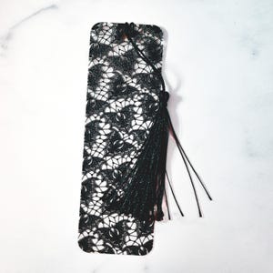 May include: Black and white lace bookmark with a black tassel. The bookmark is made of metal and has a delicate lace design.