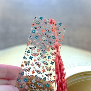 May include: A clear plastic bookmark with a colorful butterfly pattern and a red tassel. The bookmark is designed to be used with a book.