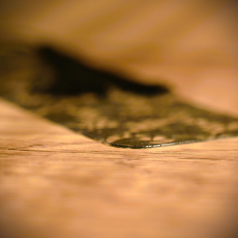 May include: A close-up of a black, rectangular, textured object on a light brown wooden surface.