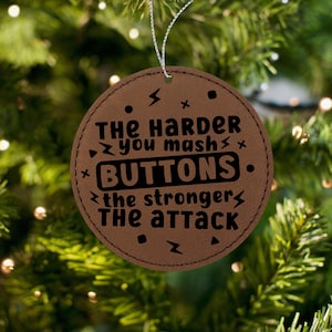 May include: Brown leather Christmas ornament with the text "The harder you mash buttons, the stronger the attack".