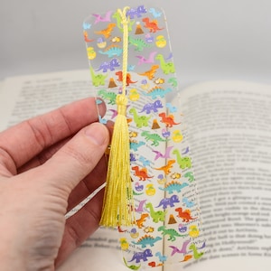 May include: A clear plastic bookmark with a colorful dinosaur pattern and a yellow tassel. The bookmark is approximately 6 inches long.