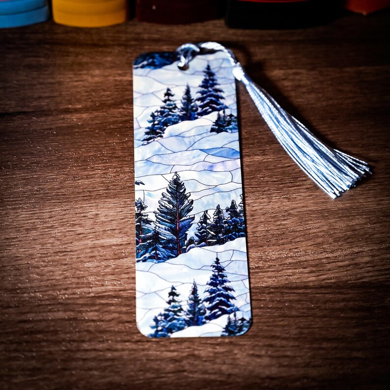May include: A blue and white bookmark with a winter scene of trees and snow. The bookmark has a blue tassel.