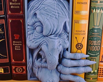 May include: A blue 3D printed bookend shaped like a witch's head with a snarling expression and a long, pointed nose. The witch's hand is reaching out with long, sharp claws.