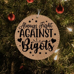 Może przedstawiać: Brązowa skórzana ozdoba z napisem "Always Fight Against Bigots" czarnymi literami. Ozdoba jest ozdobiona małymi gwiazdkami i sercami.