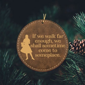 May include: A brown leather ornament with a gold silhouette of a woman and the text "If we walk far enough, we shall sometime come to someplace."
