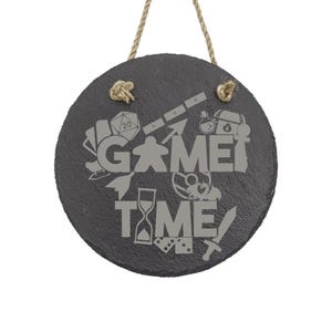 Peut inclure: Une pancarte ronde en ardoise noire avec un cintre en corde. La pancarte indique "Game Time" avec diverses ic&ocirc;nes li&eacute;es aux jeux, notamment un d&eacute;, une pi&egrave;ce de jeu, une &eacute;p&eacute;e et un sablier.