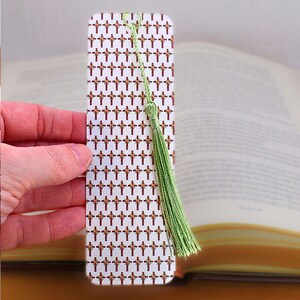May include: A white bookmark with a pattern of red crosses and a green tassel. The bookmark is being held in a hand.