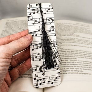 May include: A white bookmark with a black tassel and musical notes printed on it. The bookmark is about 6 inches long.