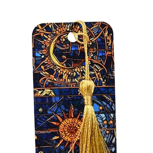 May include: A bookmark with a stained glass design featuring a sun and moon motif. The bookmark has a gold tassel.
