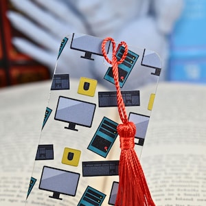 May include: A clear plastic bookmark with a red tassel. The bookmark features a repeating pattern of computer monitors, keyboards, and computer towers.
