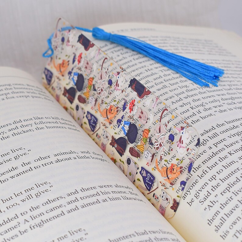 May include: A clear bookmark with a blue tassel. The bookmark features a repeating pattern of black cats, white dogs, and other animals on a white background. The text "How lat?" is visible on the bookmark.