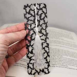 May include: A clear plastic bookmark with a white tassel. The bookmark has a black and white pattern of ghosts.