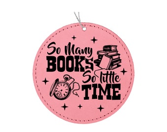 May include: Pink leather round ornament with black text that reads "So many books so little time". The ornament also features a black and white illustration of a stack of books and a pocket watch.