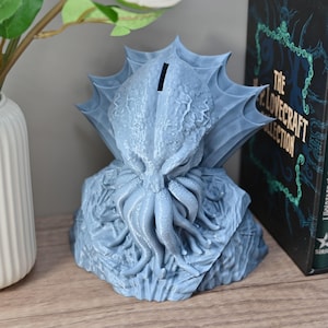 May include: A blue 3D printed Cthulhu piggy bank with a slot on the top of its head. The Cthulhu is depicted with tentacles and a menacing expression.