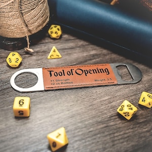 May include: A brown leather bottle opener with a metal cap opener. The bottle opener has the text "Tool of Opening" printed on it, along with the text "+1 Strength +2 vs Bottles Weight: 2.5".