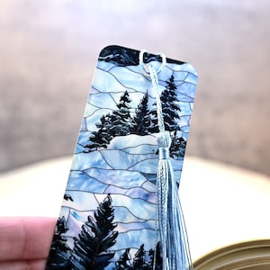 May include: A blue and white stained glass bookmark with a winter scene featuring trees and snow. The bookmark has a light blue tassel.
