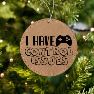 May include: A brown leather Christmas ornament with the text "I HAVE CONTROL ISSUES" and a black video game controller icon.