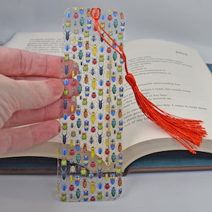 May include: A clear glass bookmark with a colorful beetle pattern and a red tassel. The bookmark is about 6 inches long and 2 inches wide.