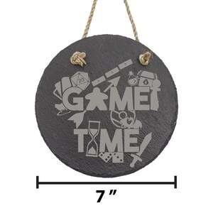 Peut inclure: Une plaque ronde en ardoise noire avec un cintre en corde. La plaque indique "Game Time" en lettres grises avec diverses ic&ocirc;nes de jeux entourant le texte. La plaque mesure 17,8 cm de diam&egrave;tre.