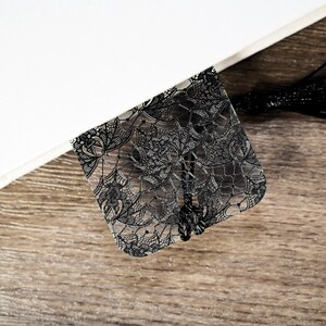 May include: Black lace bookmark with a tassel. The bookmark is made of clear plastic with a black lace design.